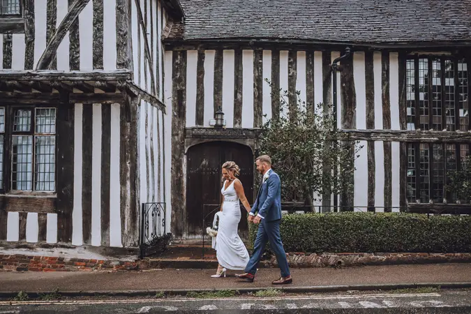 bride and groom walking hand in hand in front of 15th century building - Lottie Photography