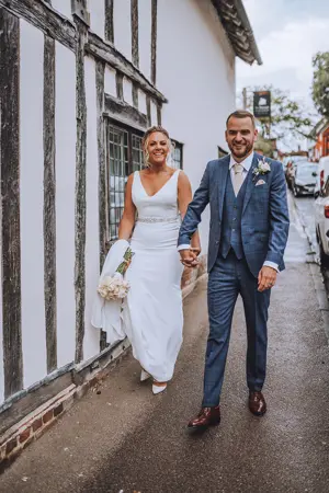 bride and groom walking hand in hand in front of 15th century building - Lottie Photography